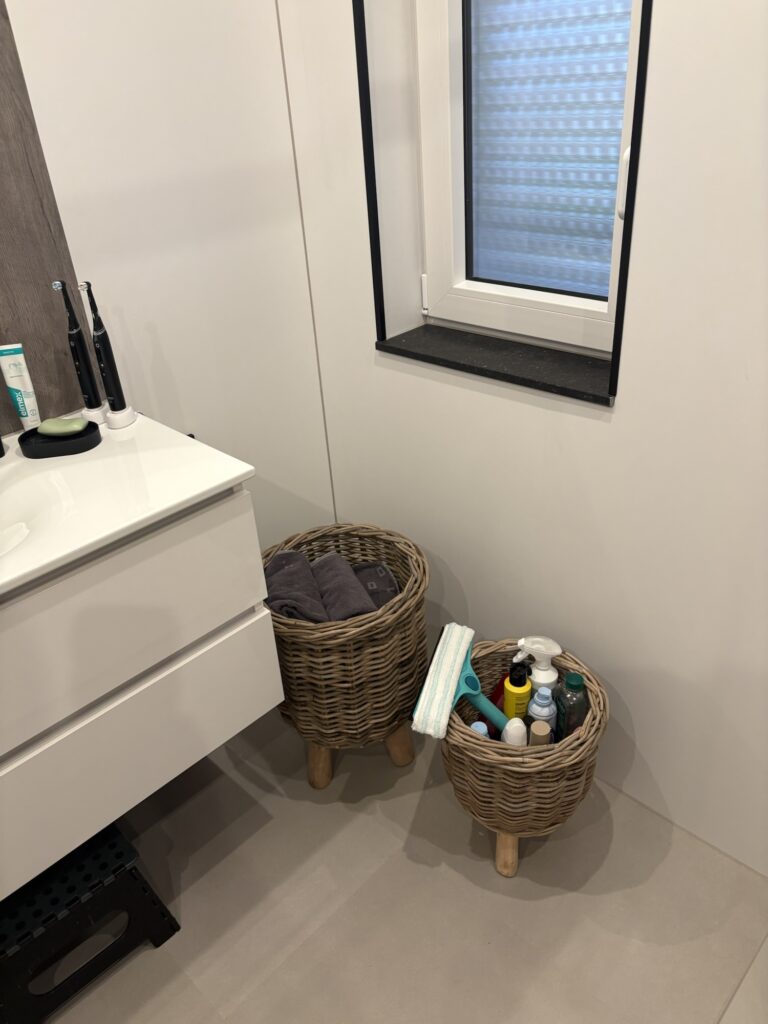 Close up of woven planter basket with wooden legs used as towel storage in a small bathroom