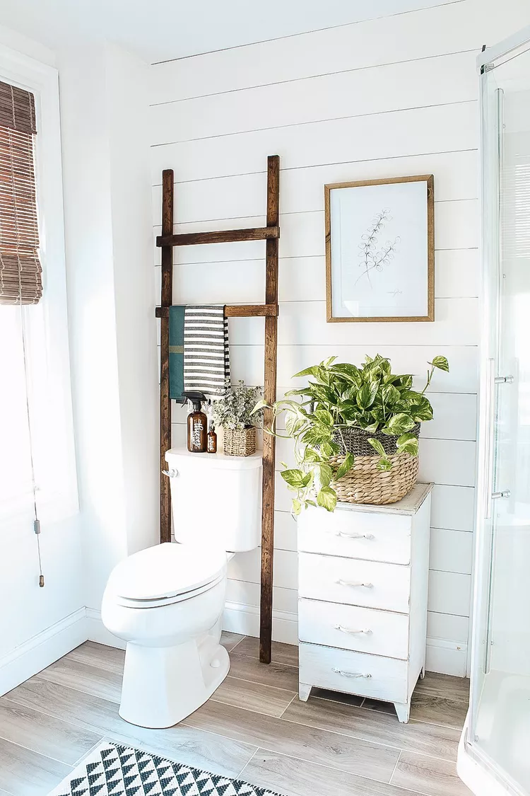 Small bathroom with over the toilet storage rack styled with towels plants and baskets