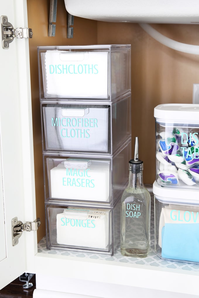 Organized under sink cabinet with stackable shelves and labeled bins