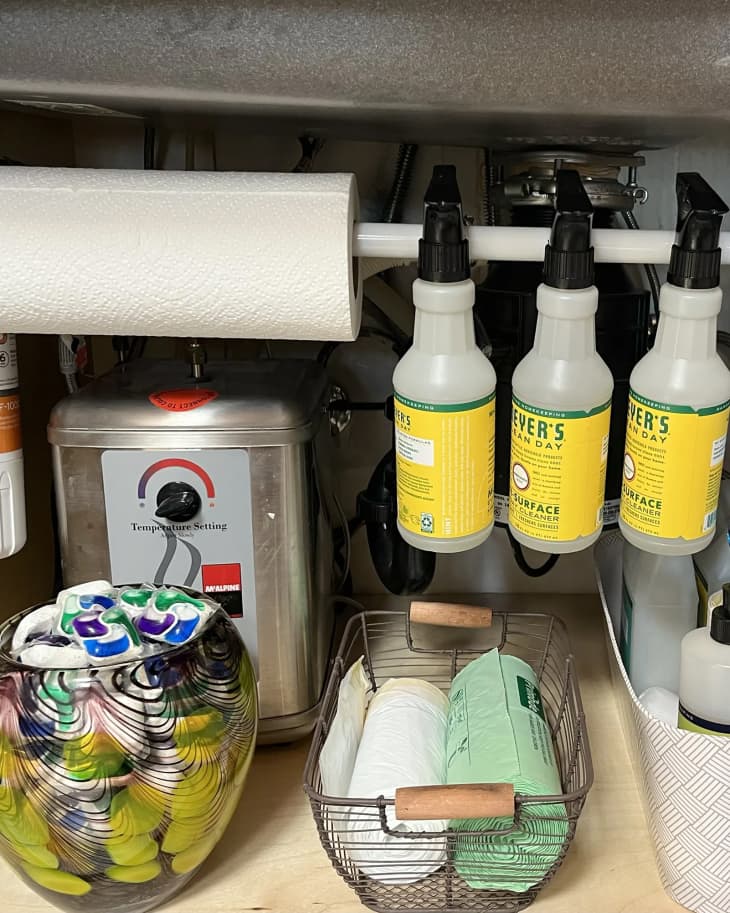 Spray bottles hanging from tension rod inside under sink cabinet