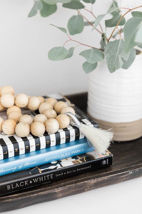 Entryway table styled with wooden beads draped over decorative books next to a ceramic vase